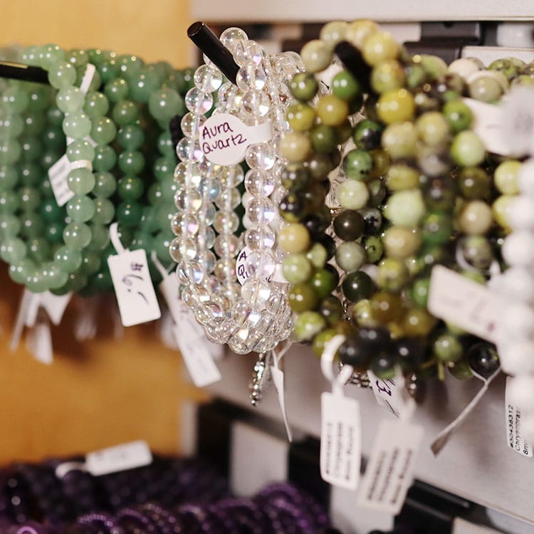 Beaded gemstone bracelets on a display rack — green aventurine, aura quartz, and jade, each with a handwritten tag