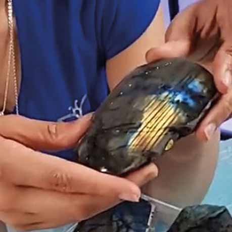 Hands holding a labradorite palm stone, showing its blue and gold flash