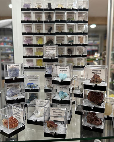 Glass shelves displaying labeled mineral and gemstone specimens from around the world at Divine Wellness